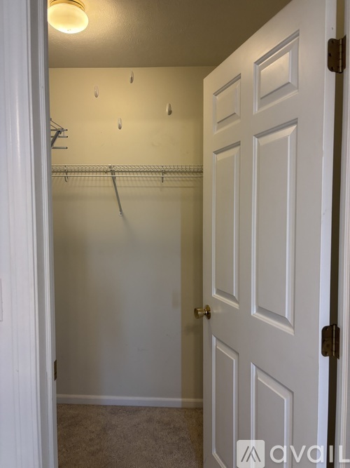 A white door with a black handle is open to a room with a white wall and a white closet with a white shelf.