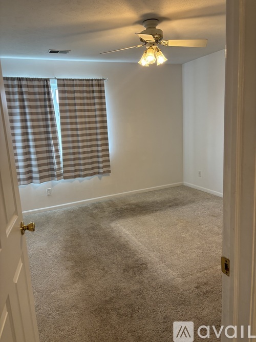 A room with a carpeted floor, a ceiling fan, and a window with curtains.