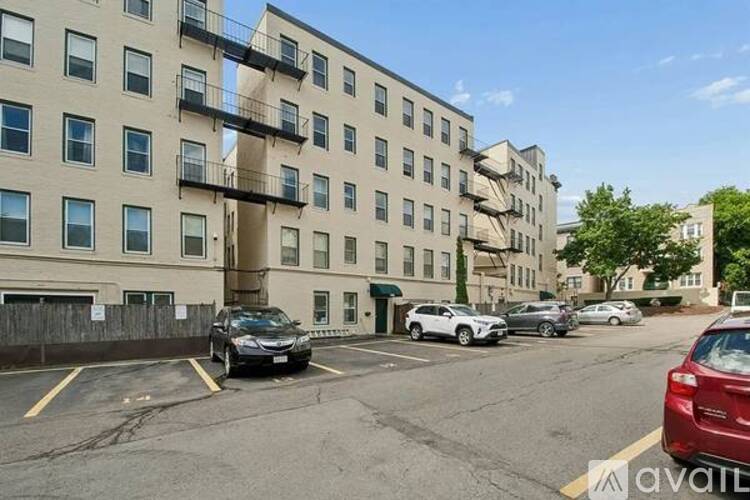 A parking lot in front of a beige apartment building with cars parked.