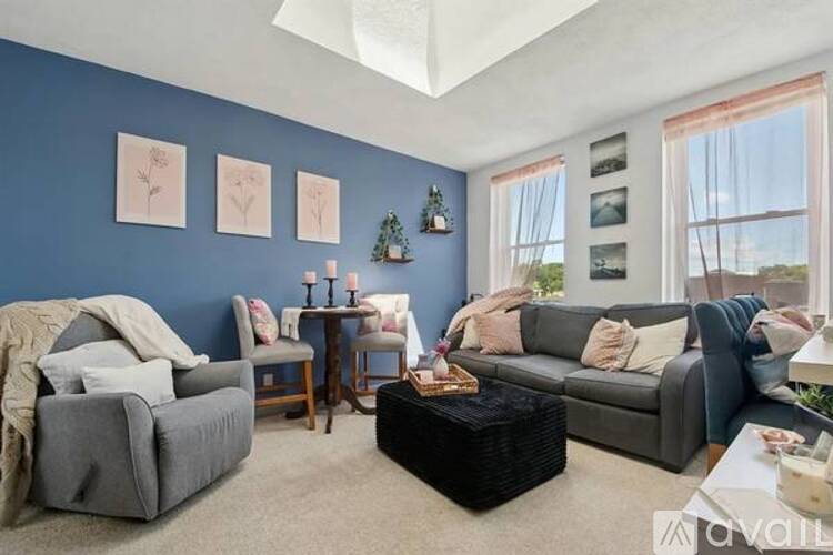 A living room with a grey couch, a grey armchair, a black ottoman, and a wooden coffee table.