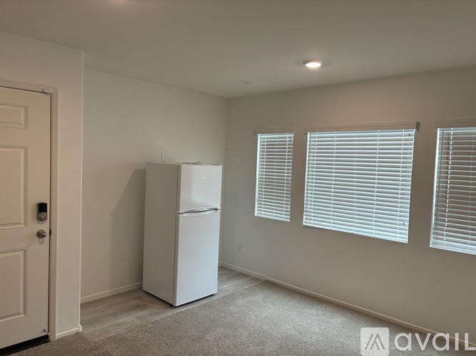 A white refrigerator is in a room with a door and two windows.