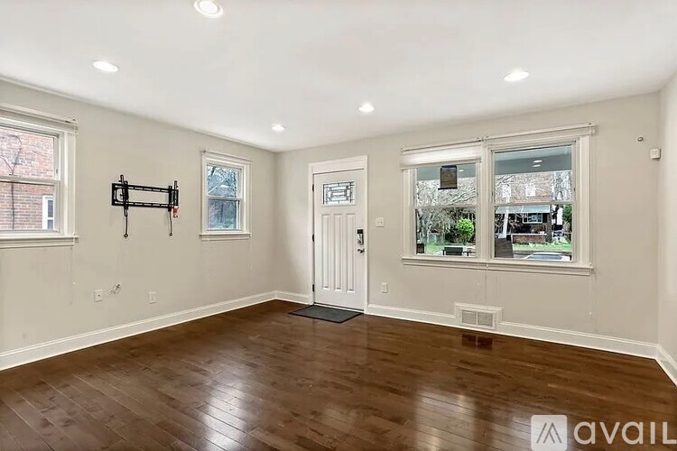 A room with wooden floors and white walls, with a door and two windows.