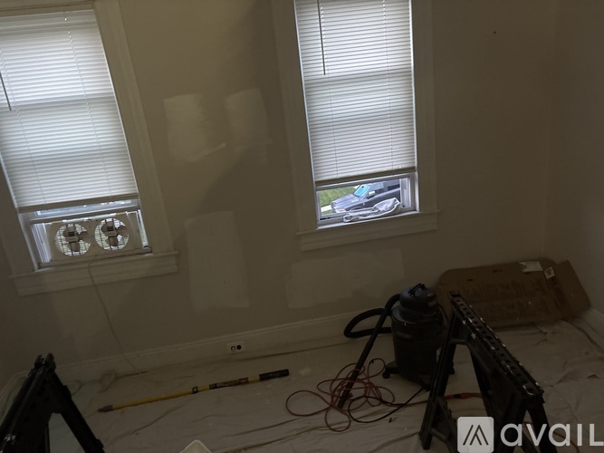 A room with two windows and a wall that is being painted white.