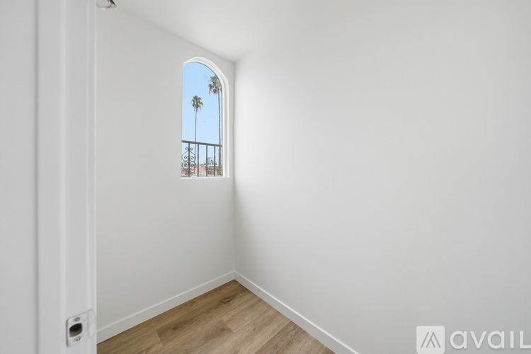 A room with a window showing a balcony with a palm tree.