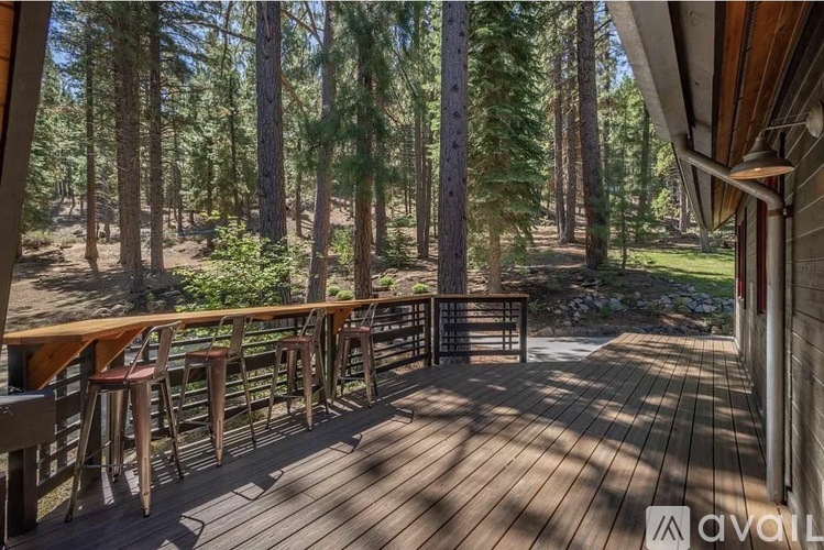 A wooden deck with stools and a railing overlooking a forest.
