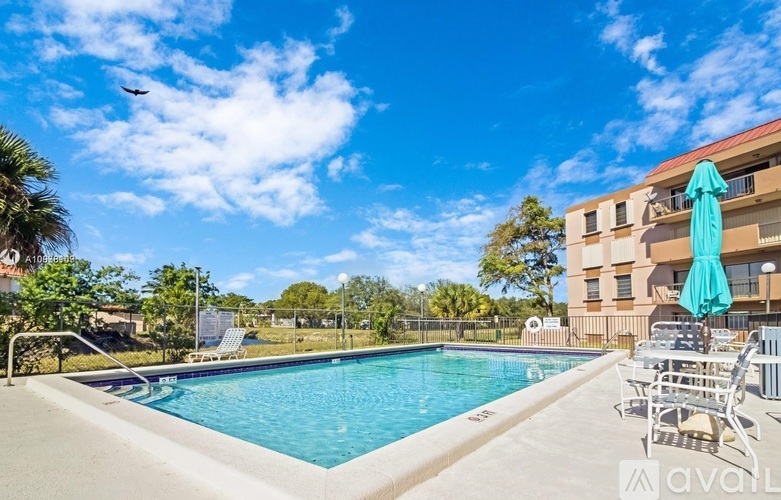 A swimming pool with a blue umbrella and chairs.