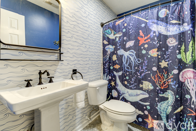 A bathroom with a white sink and toilet, a shower curtain with an ocean theme, and a blue wallpapered wall.
