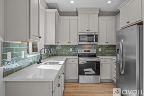 A kitchen with white cabinets and a green tile backsplash.