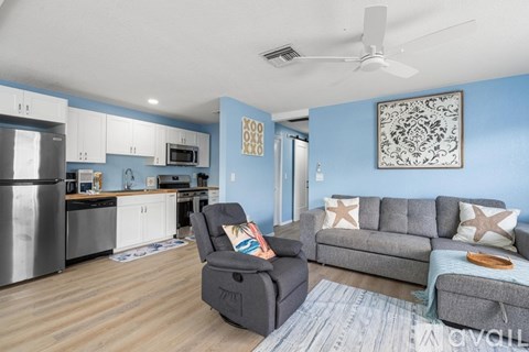 A living room with a grey couch and a kitchen area with a fridge and microwave.