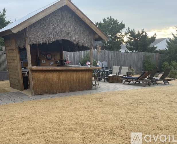 A beach hut with a thatched roof is surrounded by beach chairs.