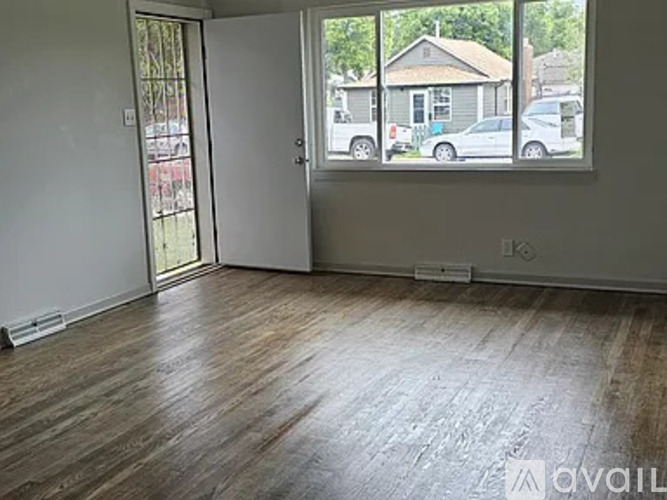 A room with wooden flooring and a large window overlooking a street.