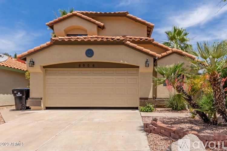 A house with a tan garage door and a black trash can in front of it.
