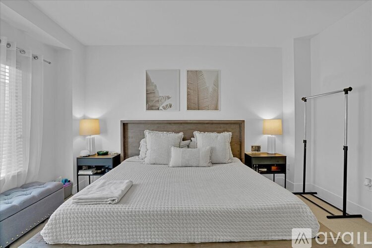A bedroom with a large bed, two lamps, and a painting on the wall.