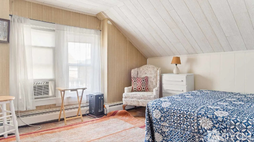 A bedroom with a bed, chair, and window.