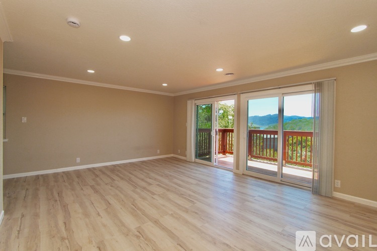 A spacious room with wooden flooring and a large window overlooking a balcony.