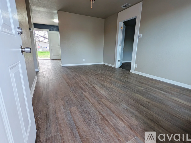 A room with wooden flooring and white walls, with a door on the left and an open door on the right.