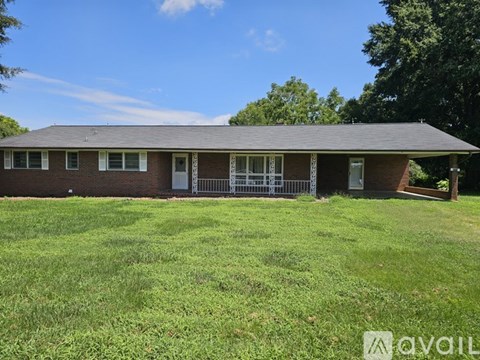 A house with a red brick exterior and a white door is surrounded by a grassy lawn.