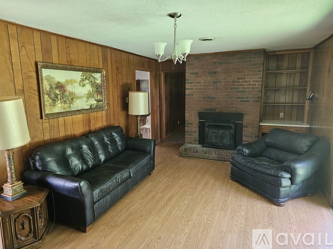 A living room with a black leather couch and chair, a lamp, a fireplace, and a painting on the wall.