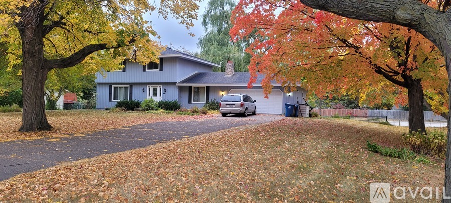 A house with a driveway and trees with fall leaves.