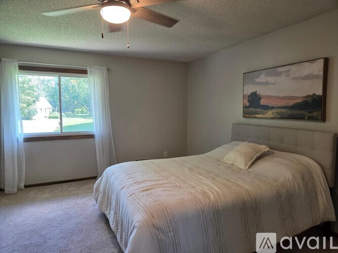 A bedroom with a bed, a ceiling fan, and a painting on the wall.