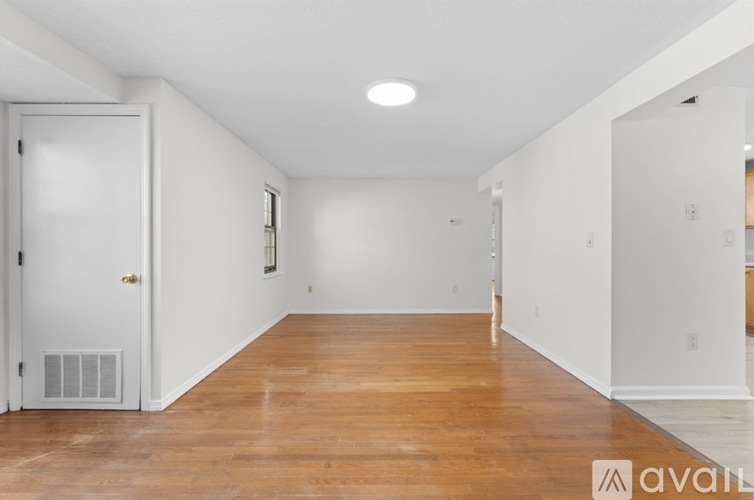 A room with wooden floors and white walls, with a door on the left and a window on the right.