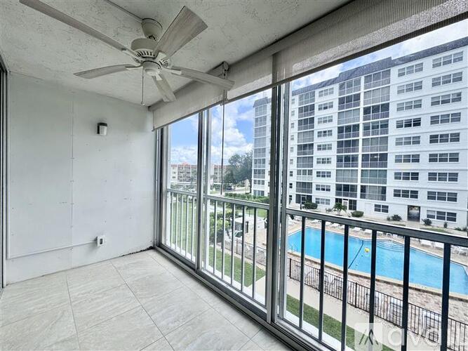 A room with a ceiling fan and a view of a pool and buildings outside.