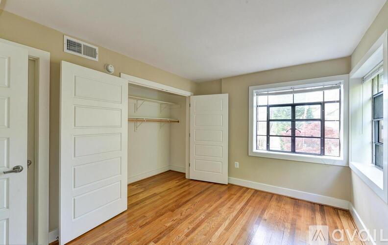 A room with a white door, a window, and a wooden floor.