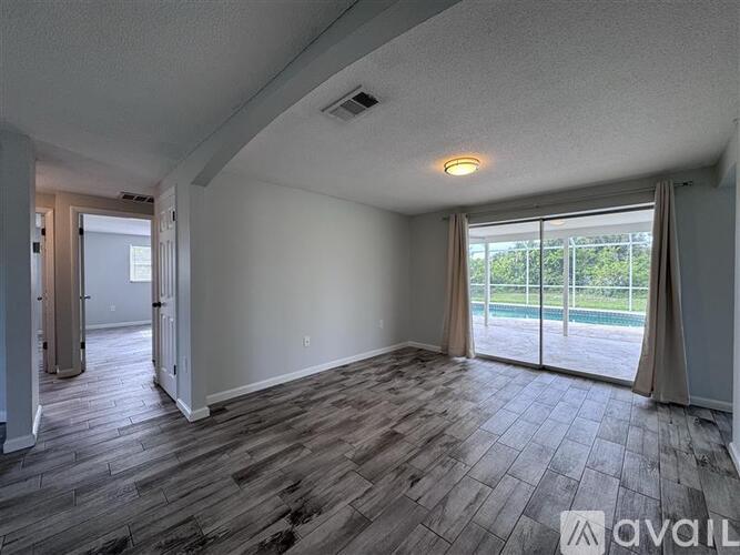 A spacious room with wood flooring and sliding glass doors leading to a backyard.