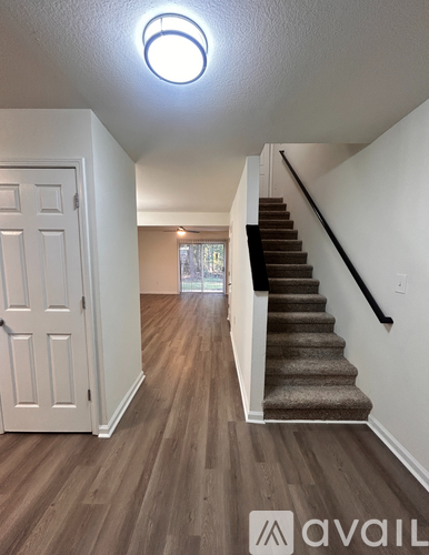 A hallway with wooden floors and a staircase with a carpeted runner.