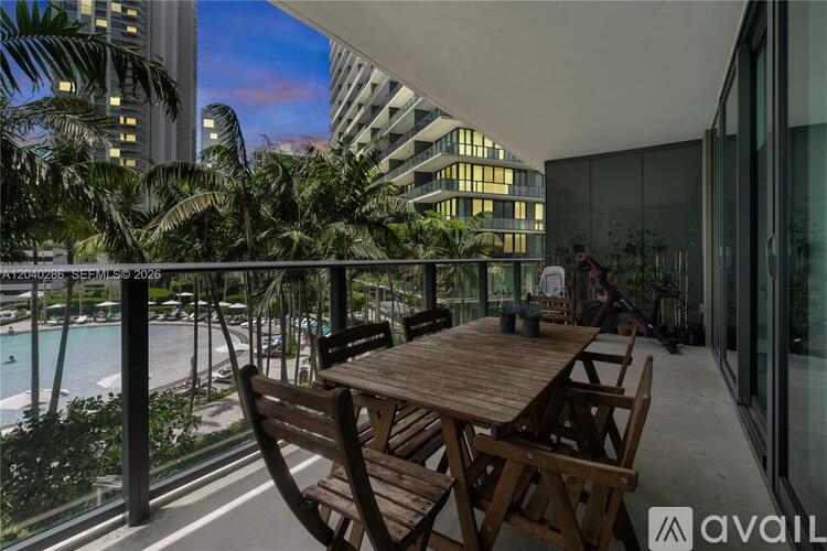 A wooden table and chairs are set up on a balcony overlooking a pool and palm trees.