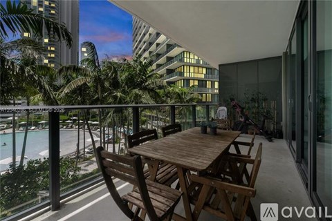 A wooden table and chairs are set up on a balcony overlooking a pool and palm trees.