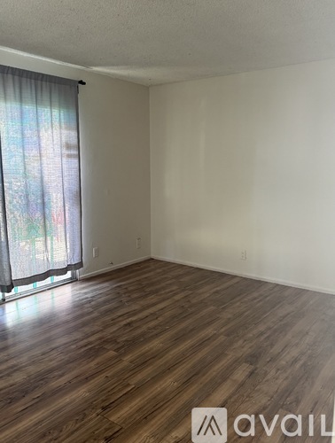 A room with wooden flooring and a window with curtains.
