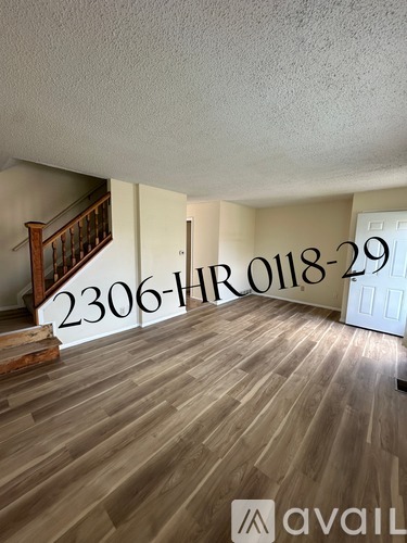 A room with wooden flooring and a staircase with a sign that reads "2306-HRO118-29" and "avail".