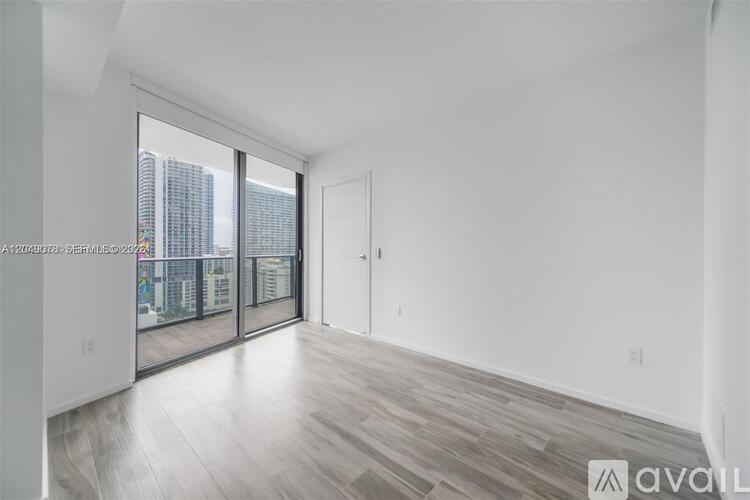 A spacious room with wooden flooring and a view of a city skyline through the windows.