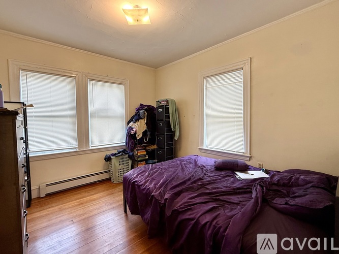 A bedroom with a purple bedspread and a window with blinds.