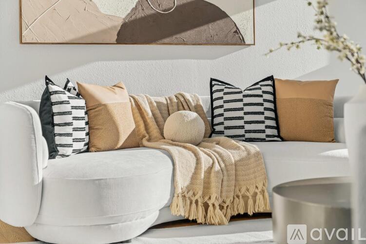 A white couch with a beige throw blanket and striped pillows.