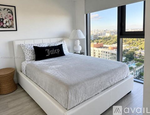 A bedroom with a large bed and a city view through the window.