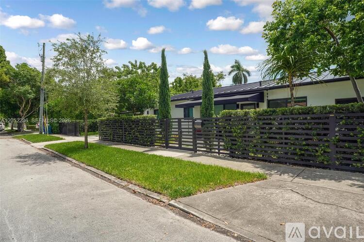 A residential street with a house, trees, and a fence.
