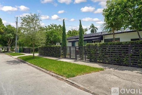 A residential street with a house, trees, and a fence.