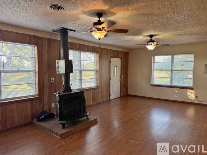 A wood stove is in a living room with a fan and a window.