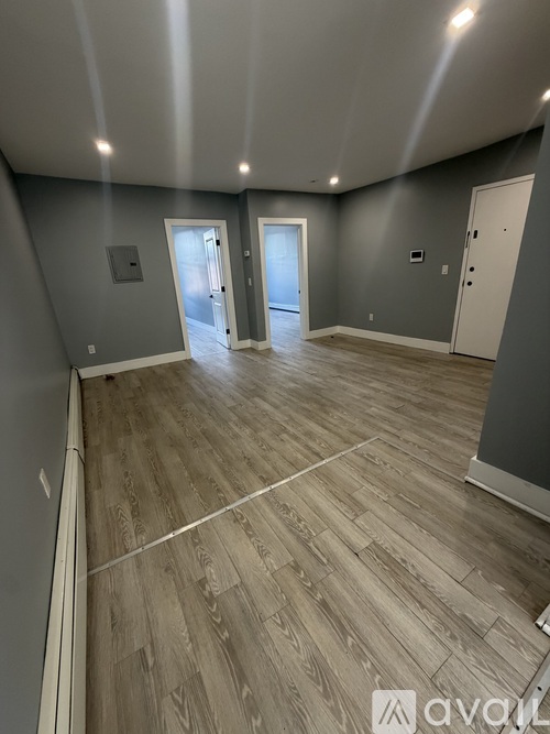 A spacious room with wooden flooring and three doors.