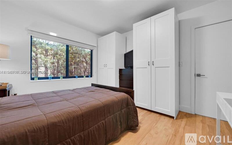 A bedroom with a bed, a TV, and a window with a view of trees.