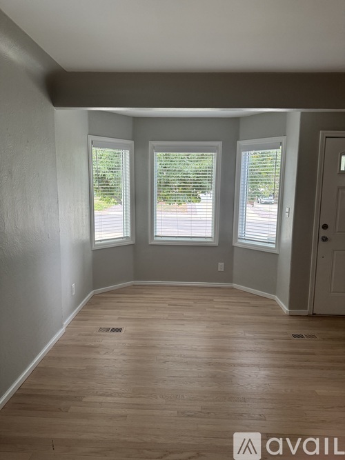 A room with wooden flooring and two windows.