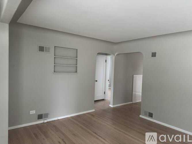 A spacious room with wooden flooring and white walls.