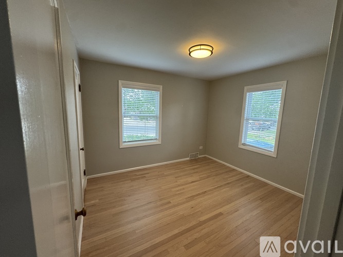 A room with wooden flooring and two windows.