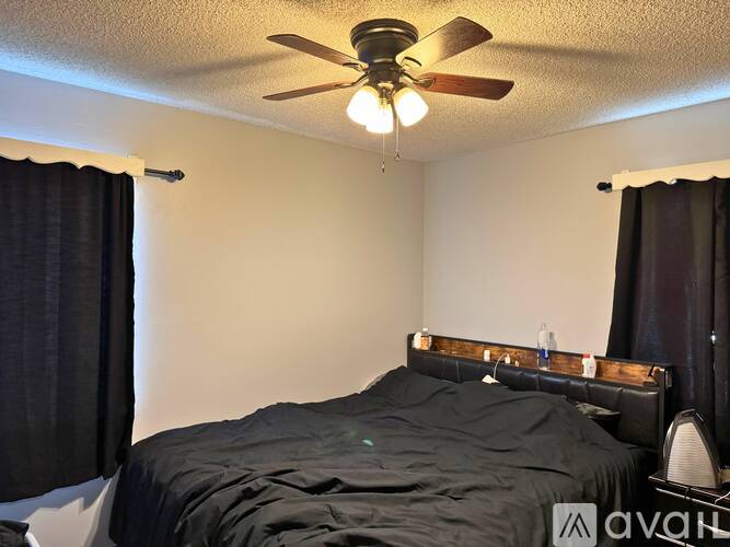 A bedroom with a bed, a ceiling fan, and a window with curtains.