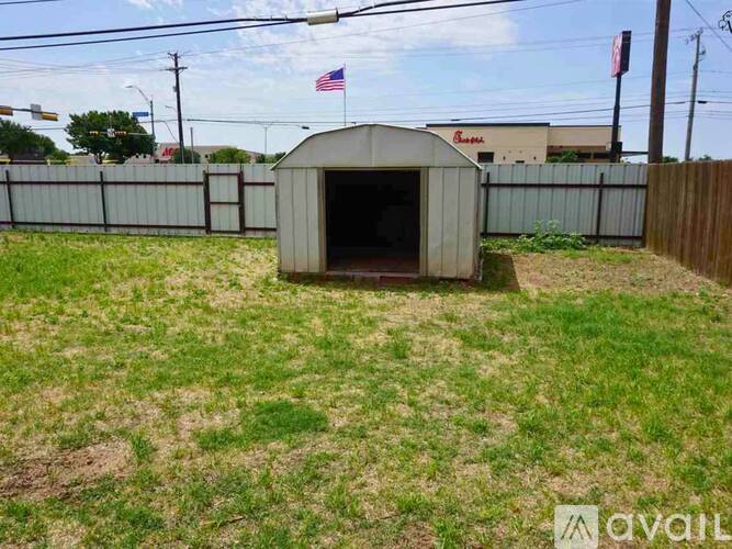 A small, white, single-story building with a brown roof is situated in a grassy area.