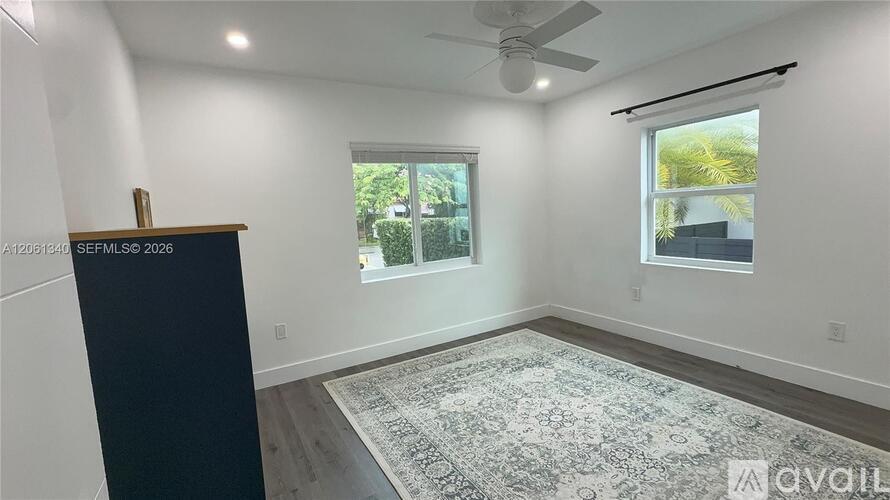 A room with a rug on the floor and a window showing greenery outside.