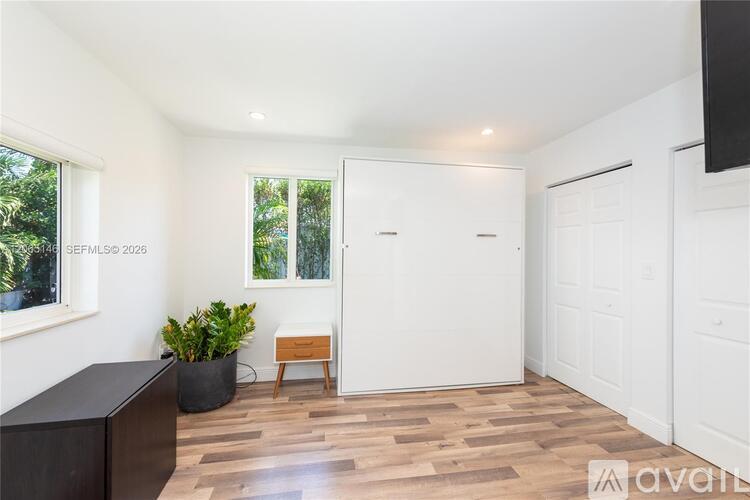 A room with a wooden floor and white walls, featuring a black cabinet, a wooden bench, and a potted plant.