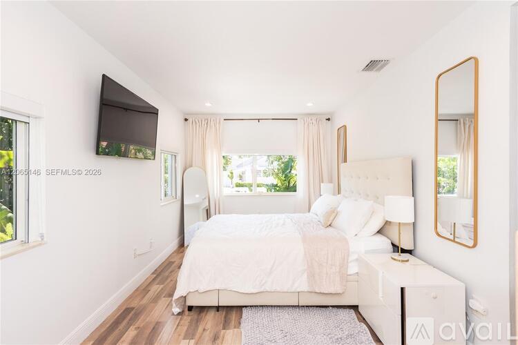 A bedroom with a large bed, a flat-screen TV, and a window with curtains.